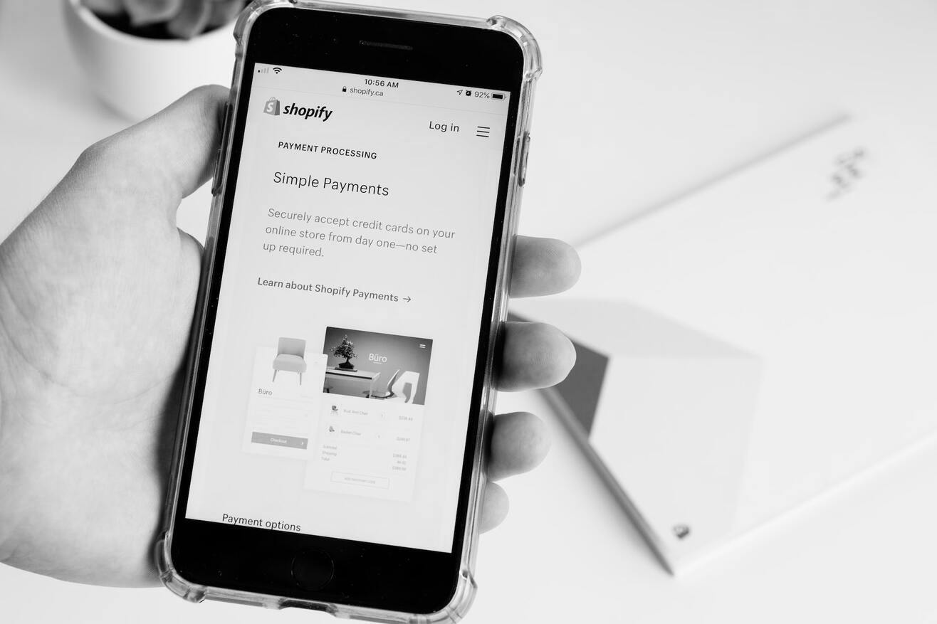 B&W image of person holding mobile showing a Shopify page