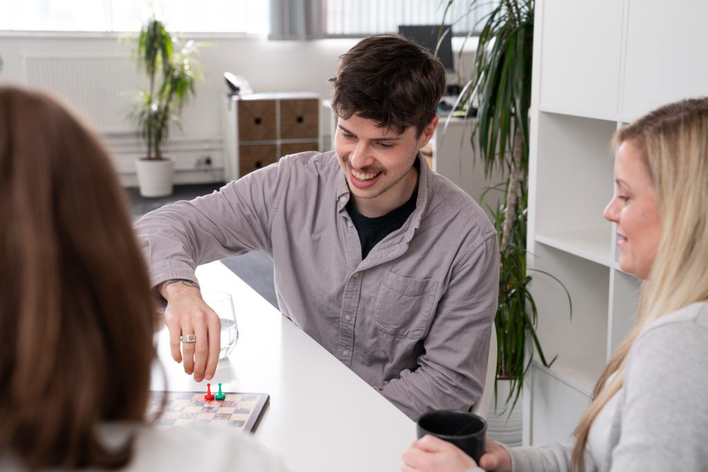 A young man sat at a large desk, playing snakes and ladders with two women