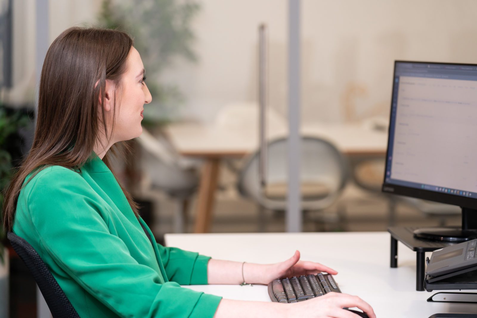 A woman wearing a green blazer, working at a computer, looking away from the camera